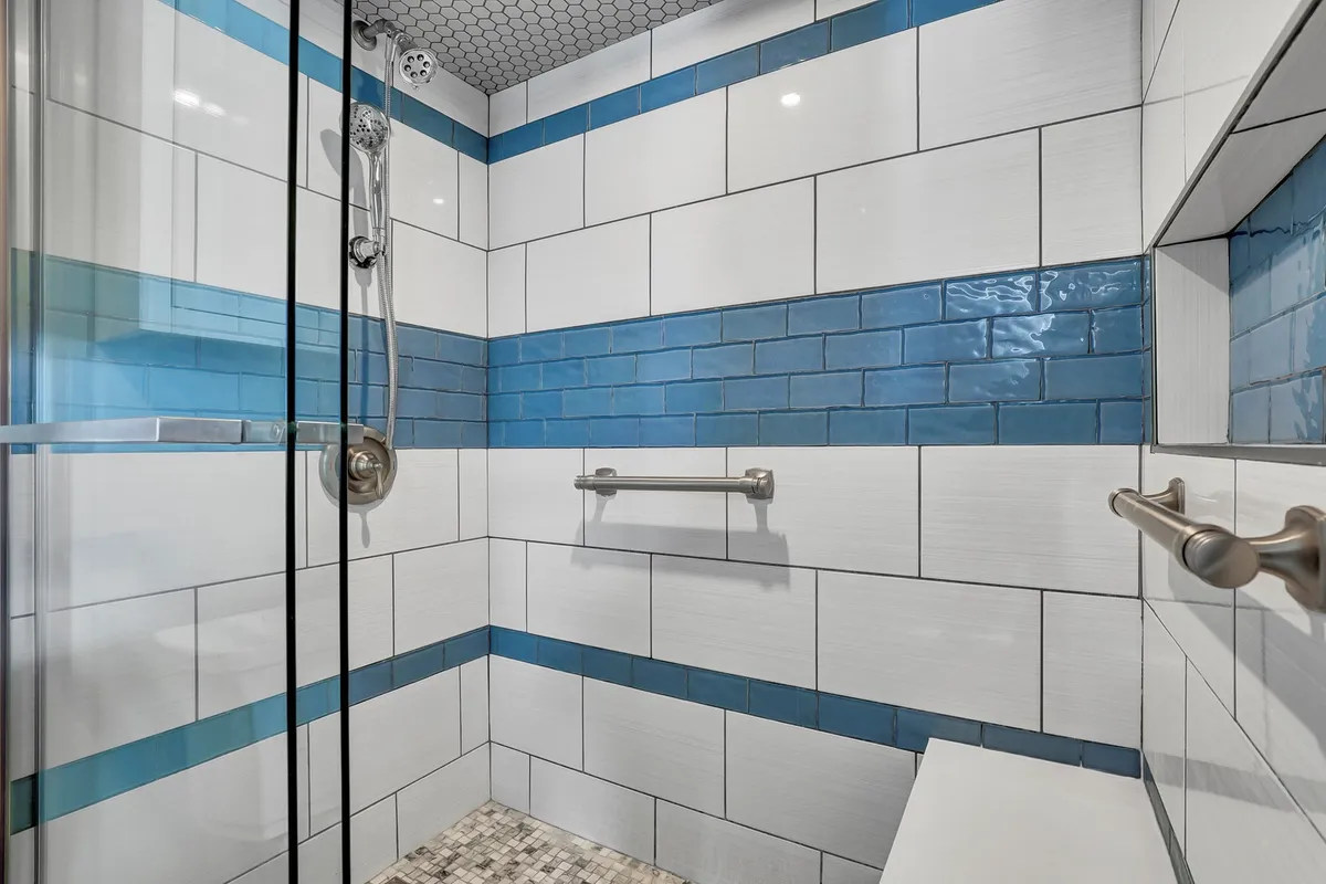A bright, updated bathroom with a glass shower enclosure and blue and white tiled walls. The space feels fresh, modern, and inviting, ideal for rejuvenating showers after a day at the beach.
