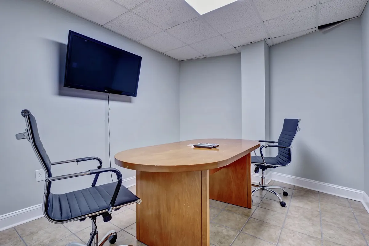 A modern business center with a wooden conference table, two office chairs, and a television screen—ideal for business meetings, work sessions, or presentations.