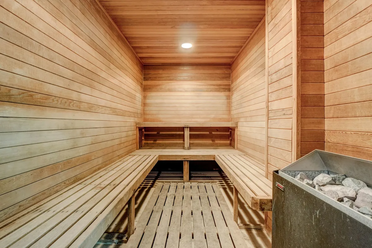 A serene sauna experience is depicted with classic wooden benches, a central sauna heater, and soft, calming lighting. The environment is perfectly set for relaxation and rejuvenation after active play or a workout session.