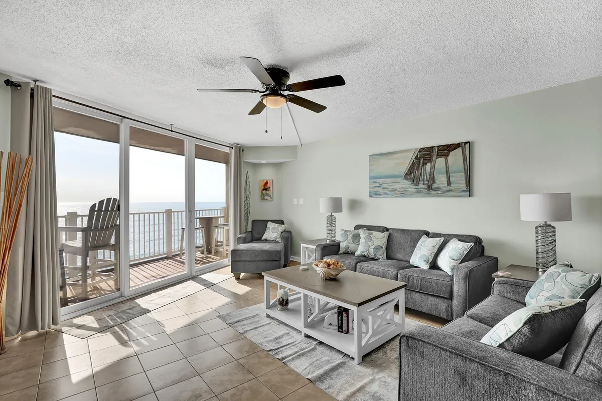 A serene interior living space featuring large windows that frame a stunning ocean view, with cozy gray sofas and a decorative coffee table creating an inviting place to relax. The soft light and peaceful setting evoke relaxation and comfort.