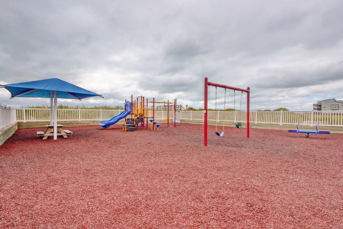 A joyful scene at the resort playground with children playing on swings and other equipment, picnic tables nearby, and a bright blue sky overhead. The area is lively and purpose-built for youthful energy and family gatherings.