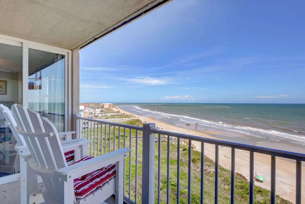 A tranquil view from a private balcony looking out over the ocean and beach, with comfortable white chairs set up for relaxation. The sky and waves create a serene backdrop, and the balcony setting suggests shared moments of relaxation across generations.