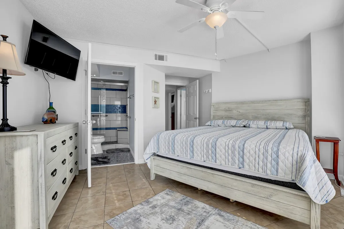 A cozy bedroom with striped bedding, a nightstand with a lamp, a wall-mounted television, and a rug. The space feels intimate, ideal for relaxation and unwinding.