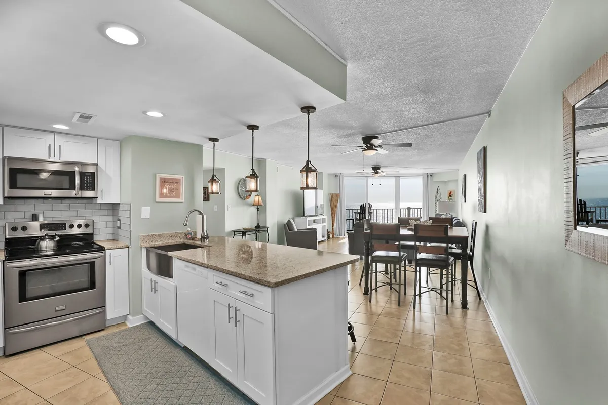A stylish kitchen and dining space featuring a central island, elegant dining table, and expansive windows overlooking the water. The kitchen is modern with visible stainless steel appliances and quartz countertops, seamlessly integrated with the dining area for open-plan living.