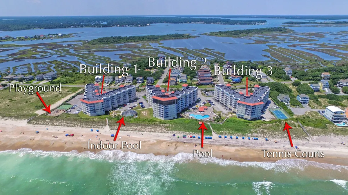 A wide exterior view of the resort grounds featuring multiple buildings, inviting swimming pools, a colorful playground, and tennis courts, all framed by beach and ocean backdrops. Families can be seen enjoying various activities around the property.