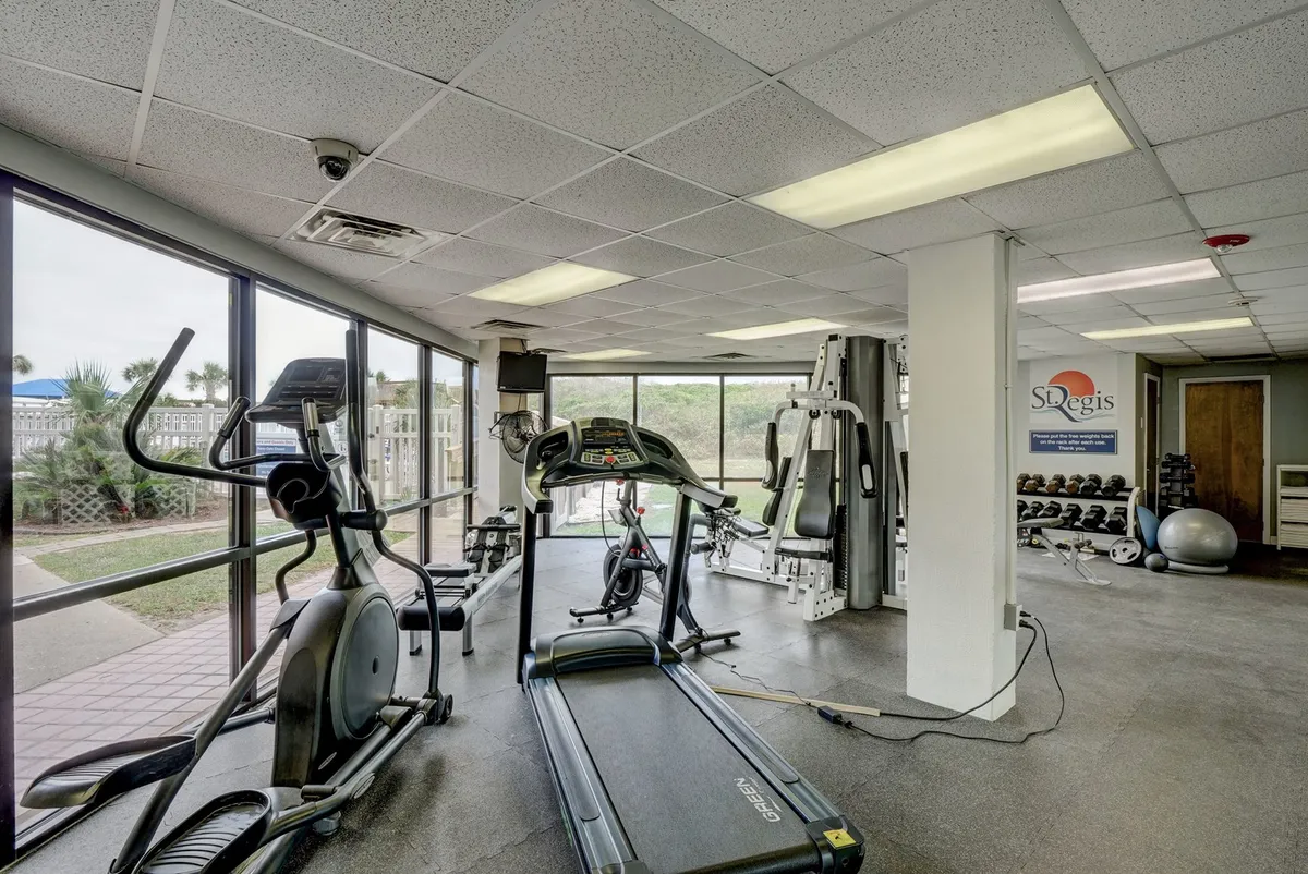 A well-equipped fitness center featuring a treadmill, elliptical machine, and weight training equipment. Large windows allow natural light to flood the space, creating an energetic and health-focused environment perfect for workouts and personal training sessions.