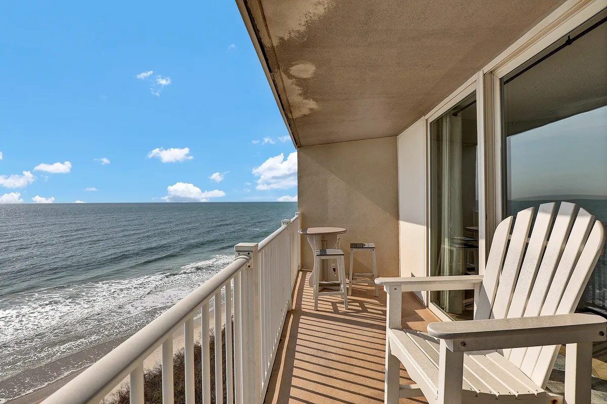 An exterior beachfront scene with a white Adirondack chair and a small side table, inviting relaxation and reflection while enjoying the ocean breeze and sunrise.