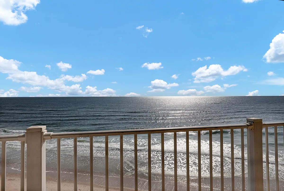 A sweeping view of the ocean and sky framed by a balcony railing, suggesting opportunities for beach walks, relaxing by the water, or simply soaking in the sunrise and serene coastal atmosphere.