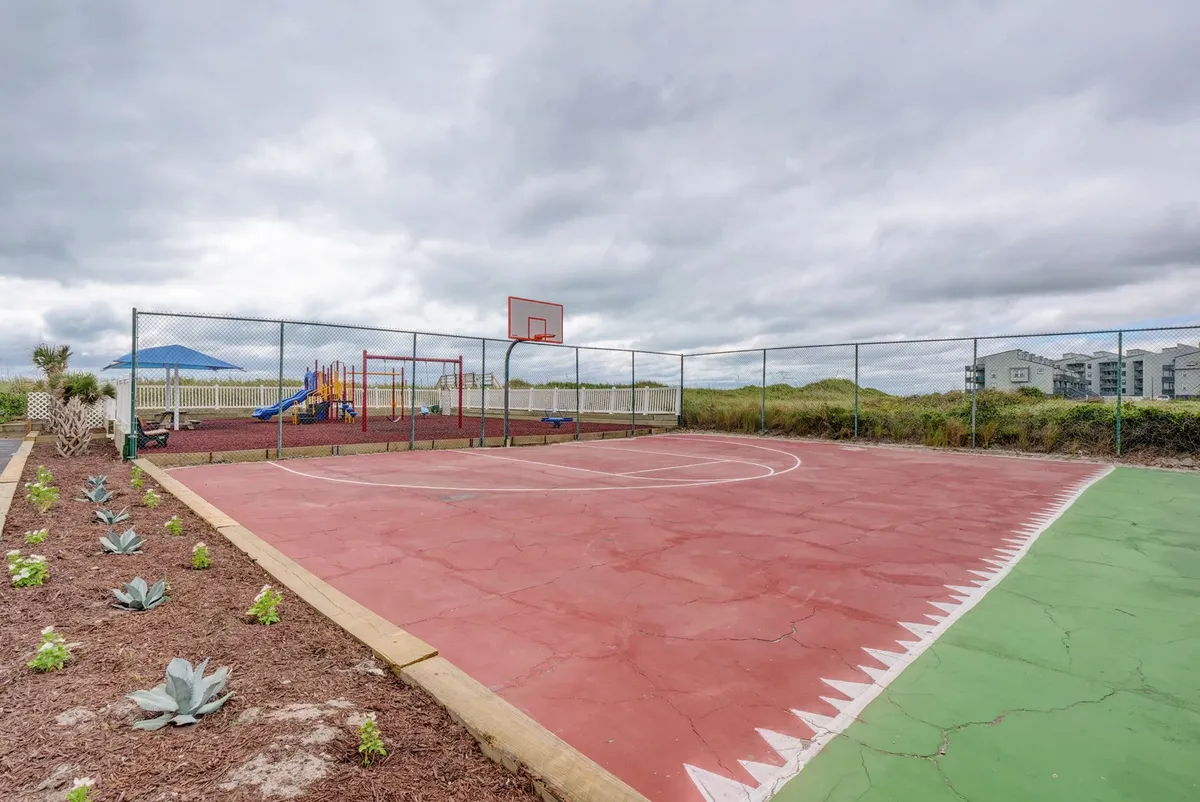 Overlooking the basketball court and playground equipment, this exterior scene captures people engaging in basketball games, children playing, and families gathering in a landscaped garden setting. The space is lively and energetic, highlighting active recreation and family fun.
