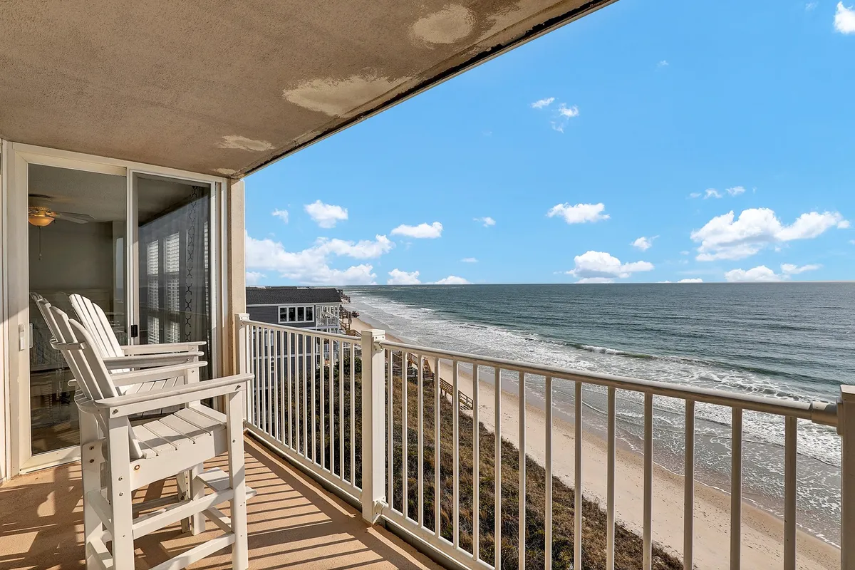A tranquil balcony scene overlooking the ocean, featuring comfortable balcony chairs facing the sand beach and Atlantic waves. The serene setting is bathed in early morning light, perfect for enjoying a coffee or quiet conversation as the sun rises.