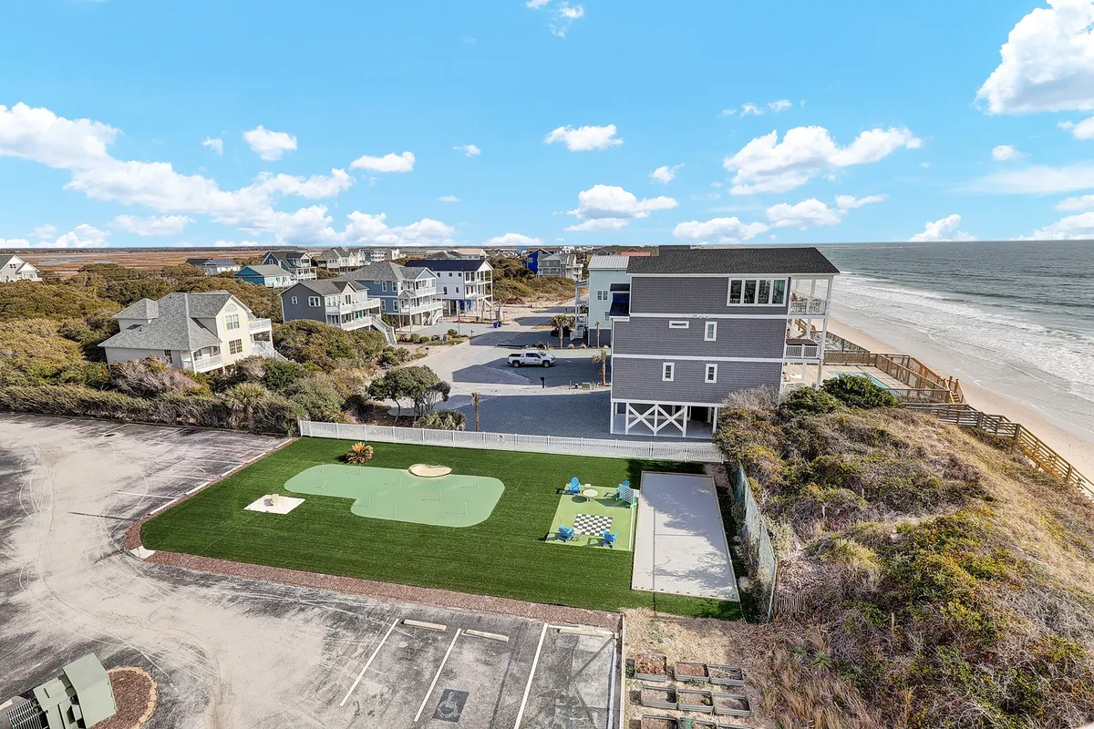 This image features an exterior scene showcasing a beach, a golf putting green, a picnic area, and an expansive ocean view. The setting is relaxed and inviting, highlighting outdoor activities and the shared enjoyment of recreational amenities just steps from the condo.