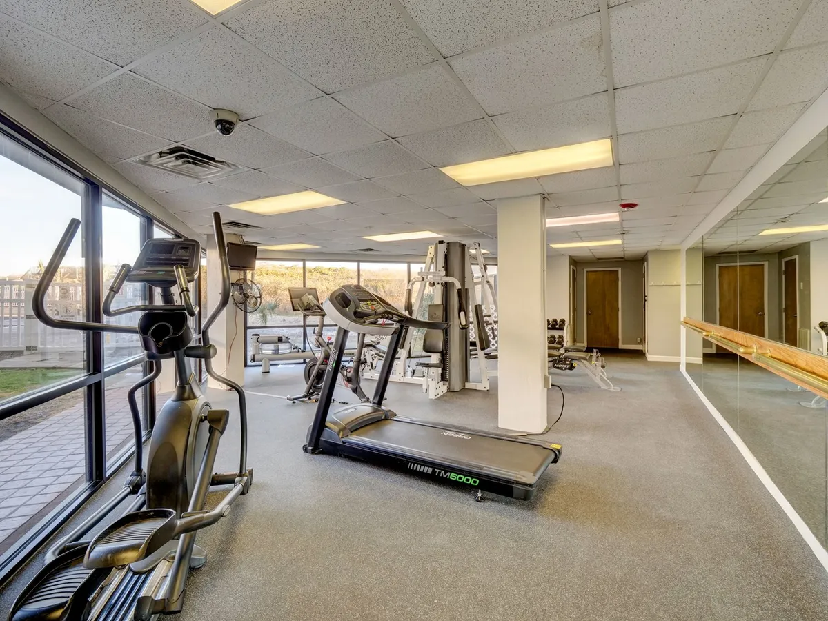 A modern, well-equipped fitness center with treadmills, elliptical machines, weight training equipment, and large windows that bring in natural light. The setting encourages motivation and health-focused activities, showing people during workouts and fitness classes.